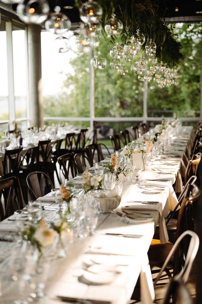 A breathtaking wedding reception setup showcasing a room adorned with large windows and an exquisite floral suspension, enhancing the elegant and light-filled atmosphere of the event.